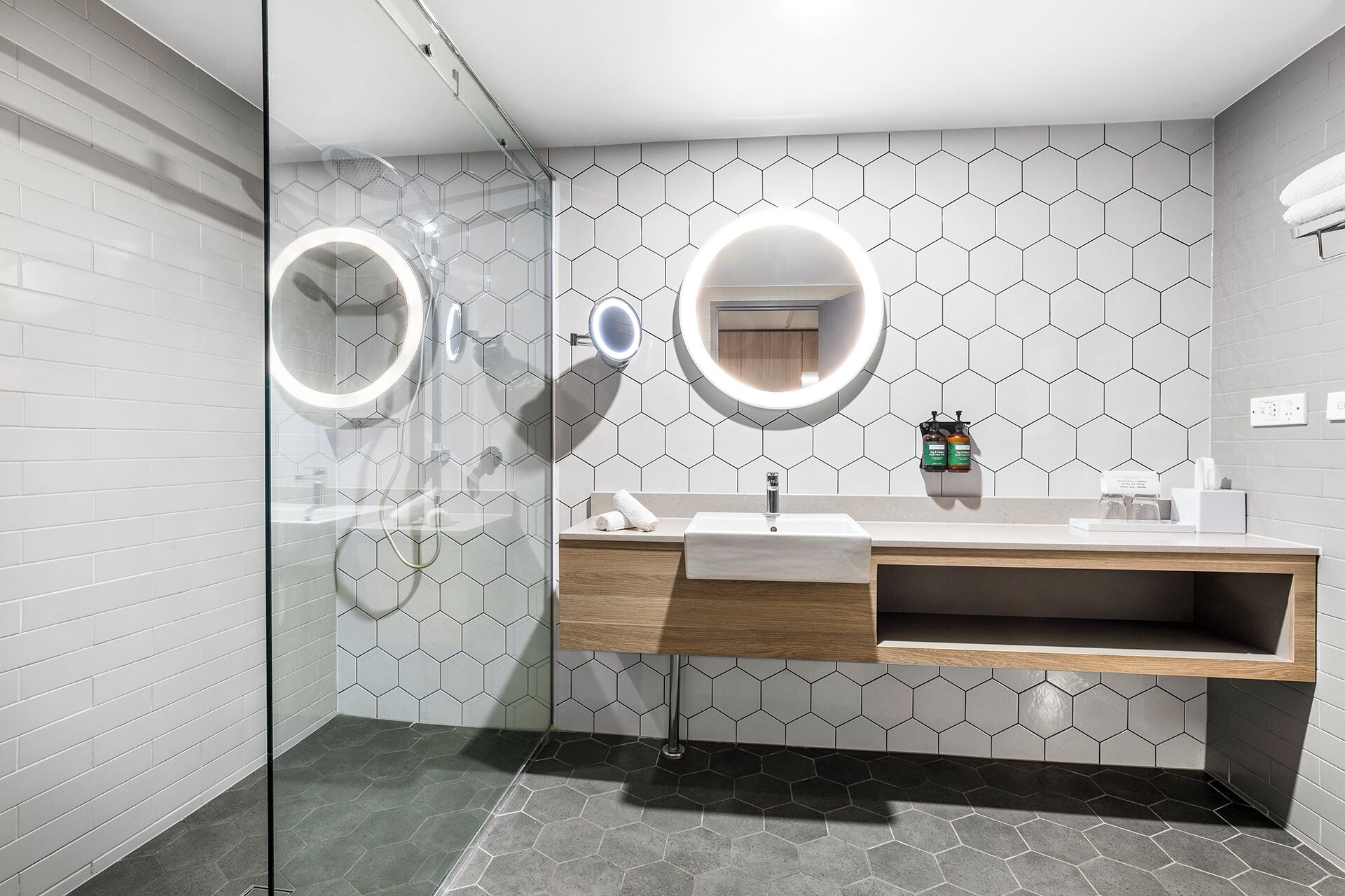 Casa de banho moderna com cabine de duche em vidro, toucador com espelho e painel de azulejos hexagonais.