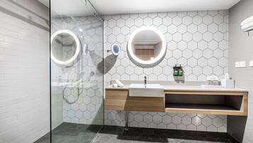 Casa de banho moderna com cabine de duche em vidro, toucador com espelho e painel de azulejos hexagonais.