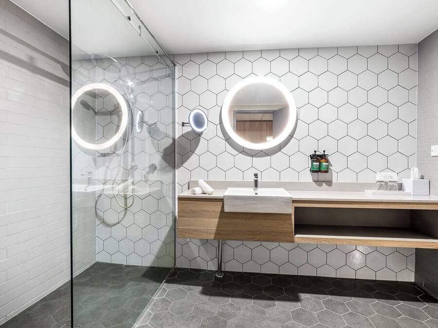 Casa de banho moderna com cabine de duche em vidro, toucador com espelho e painel de azulejos hexagonais.