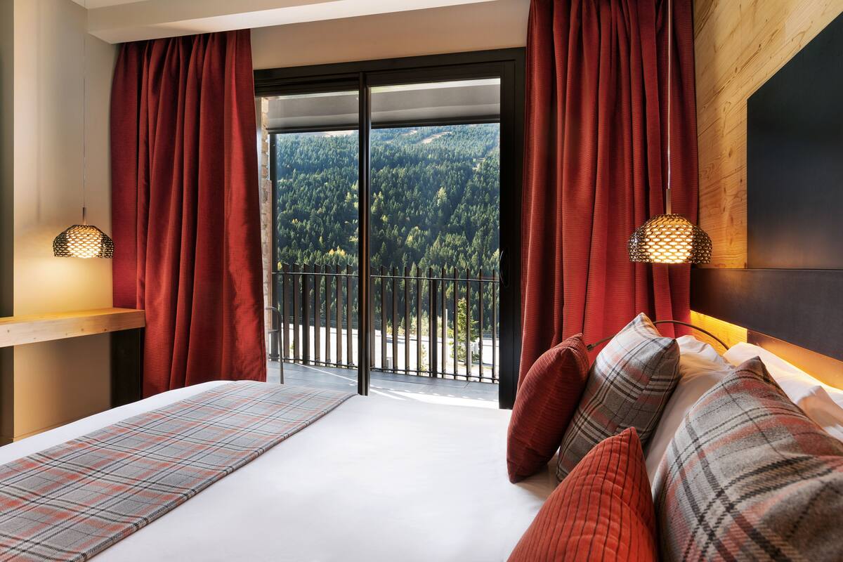 A bedroom with a large window, a bed with plaid bedding, and a view of a forest.