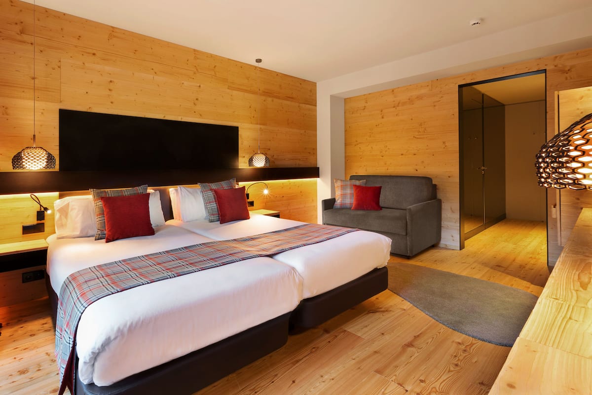 A modern bedroom with a large bed, a sofa, wooden walls, and a flat-screen TV.
