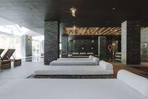 Un moderno espacio de spa con un amplio sofá blanco, sillones de madera y una pared de piedra.