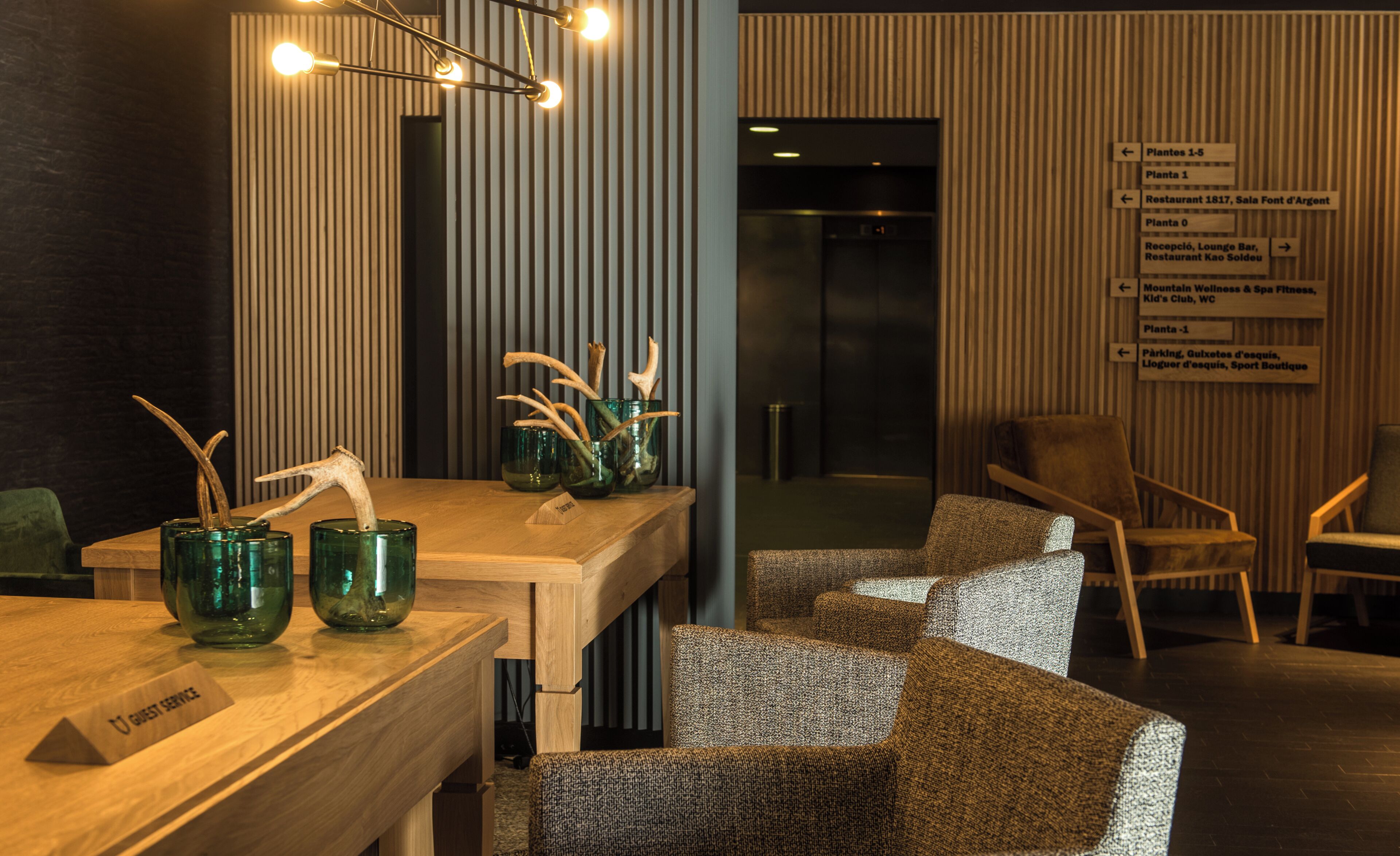 A modern hotel lobby with a reception desk, seating area, and directional signs.
