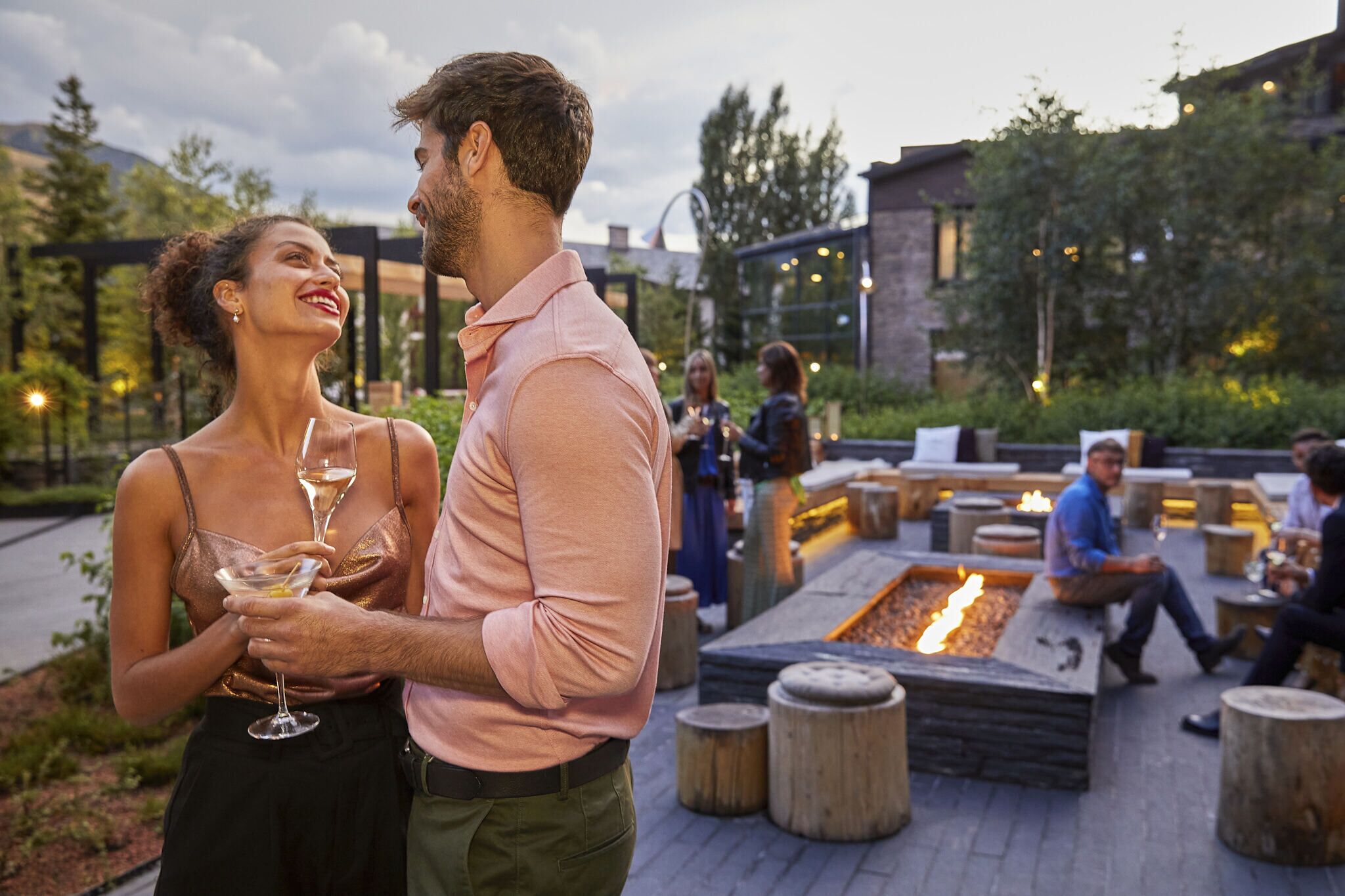 Un couple se tient à l'extérieur, avec un foyer et des espaces de détente en arrière-plan.