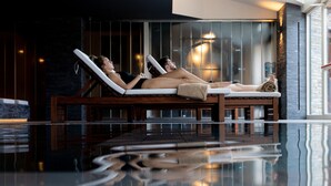 A modern indoor pool area with lounge chairs and a glass ceiling.