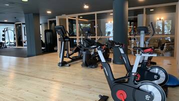 Un gimnasio con equipamiento de ejercicio, suelo de madera y ventanas amplias.