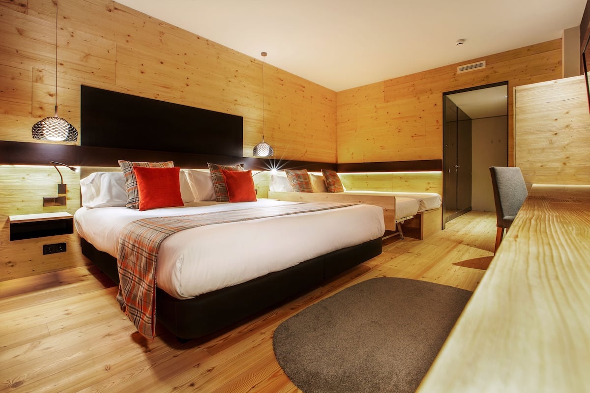 A modern bedroom with a large bed, bedside tables, a flat-screen TV, and a wooden floor.