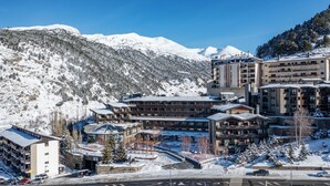 A multi-story hotel with a ski lift visible in the background, surrounded by snow-covered mountains.