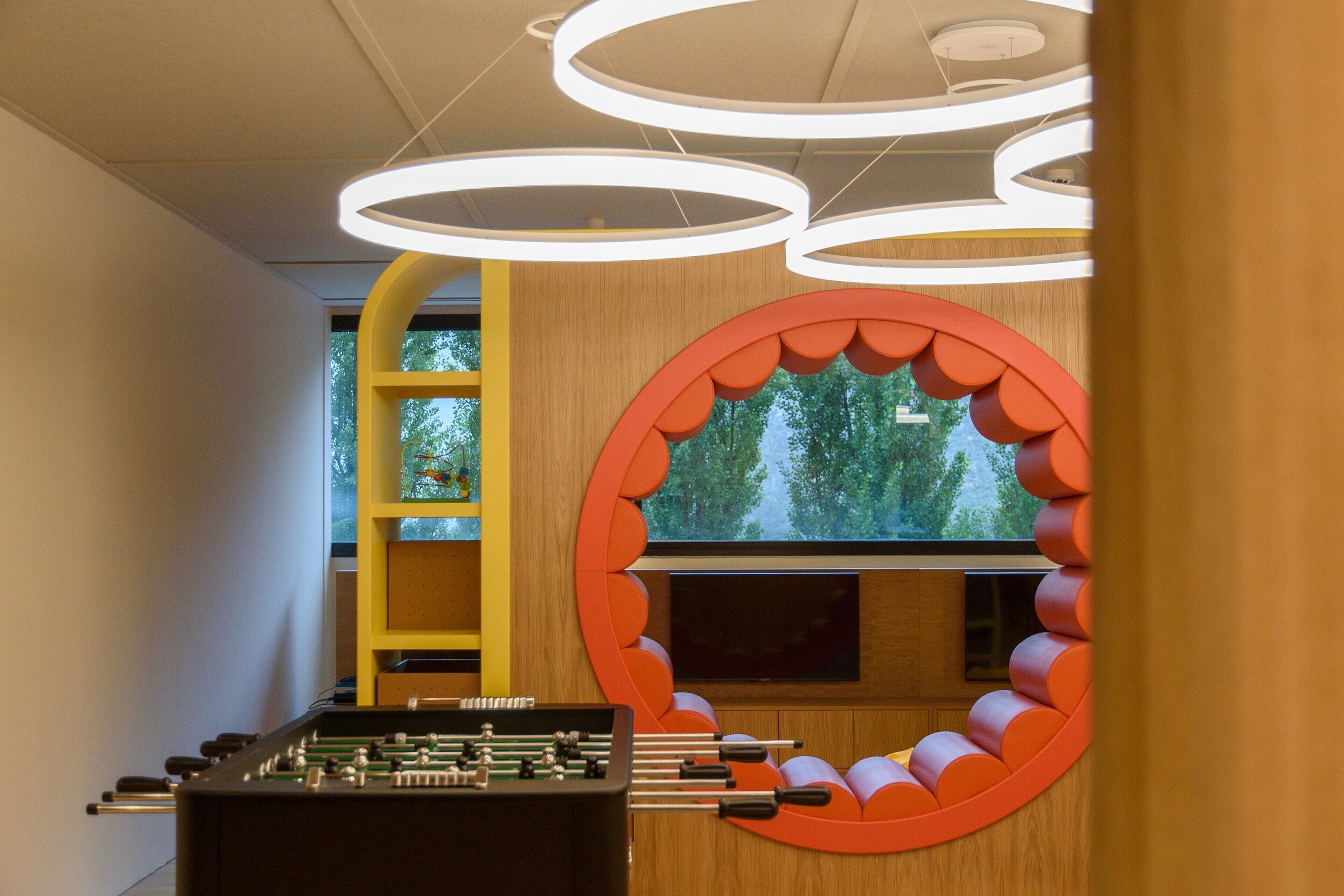 Una habitación moderna con una mesa de fútbol, un amplio ventanal circular y un diseño de techo original.