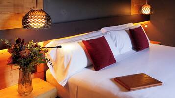 A neatly made bed with white and red pillows, a vase with flowers, and two hanging lamps.
