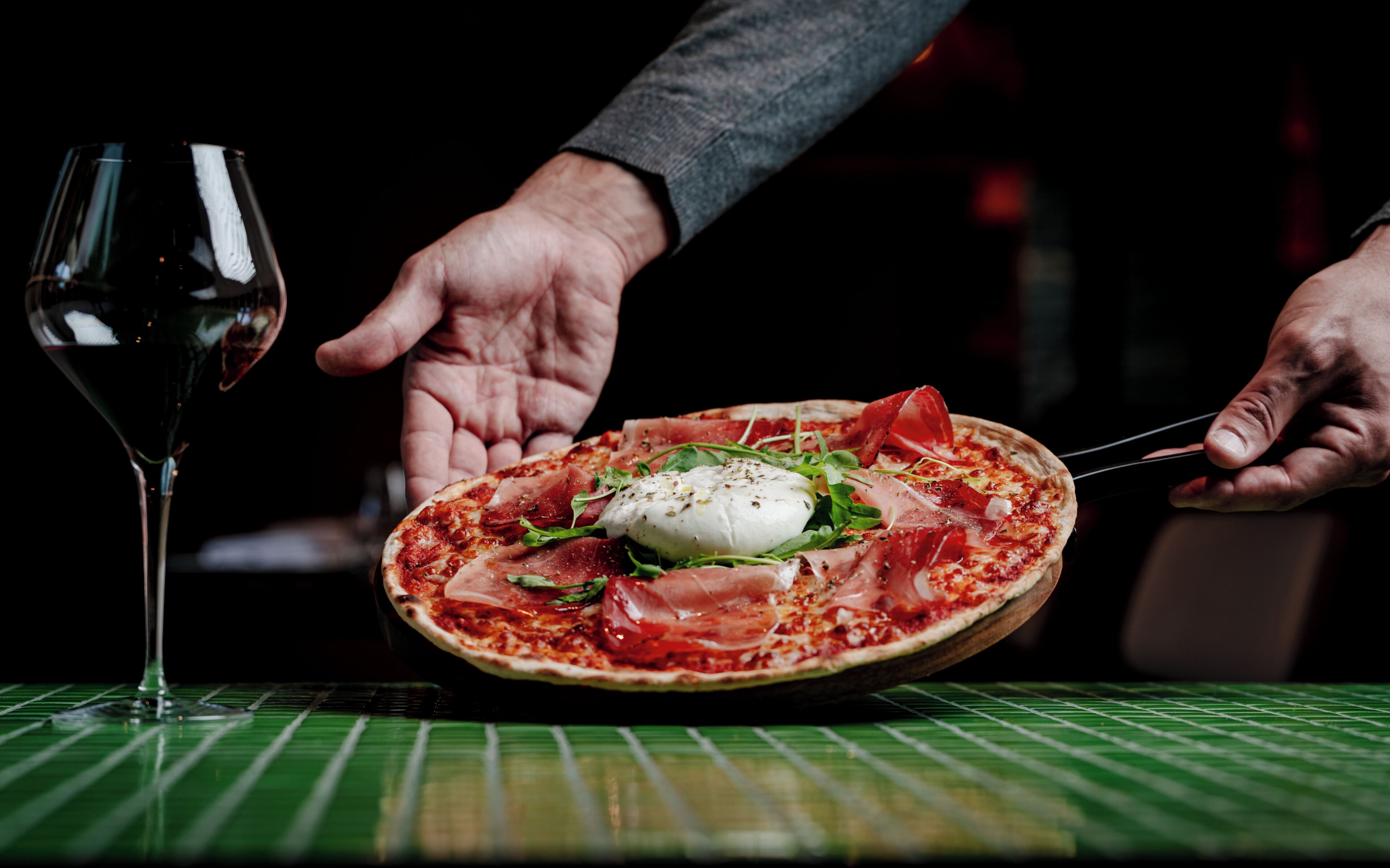 Pizza con huevo pochado, prosciutto y rúcula sobre un mantel verde.