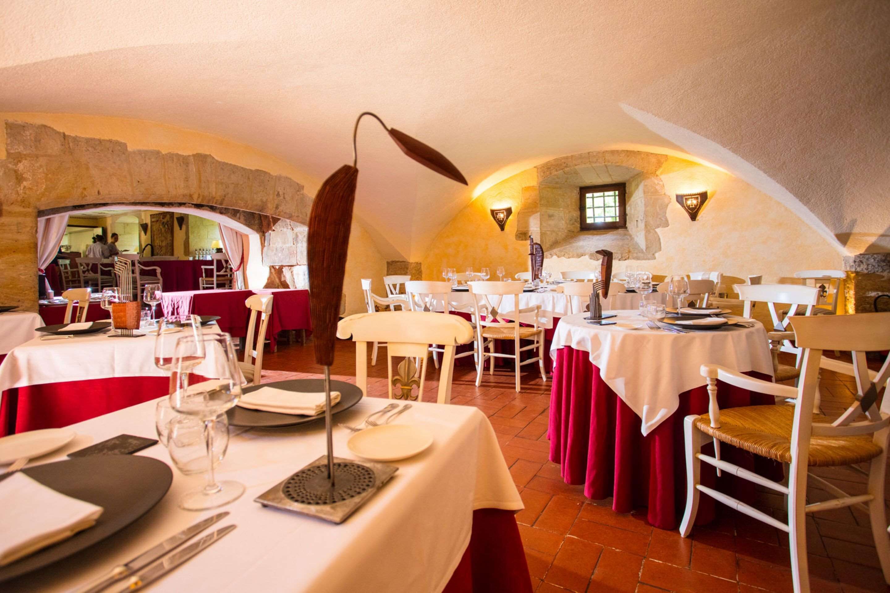 Een restaurant met witte tafels en rode gordijnen, stenen muren en een rustiek interieur.