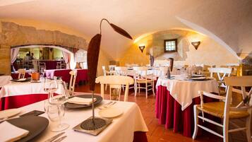 Een restaurant met witte tafels en rode gordijnen, stenen muren en een rustiek interieur.