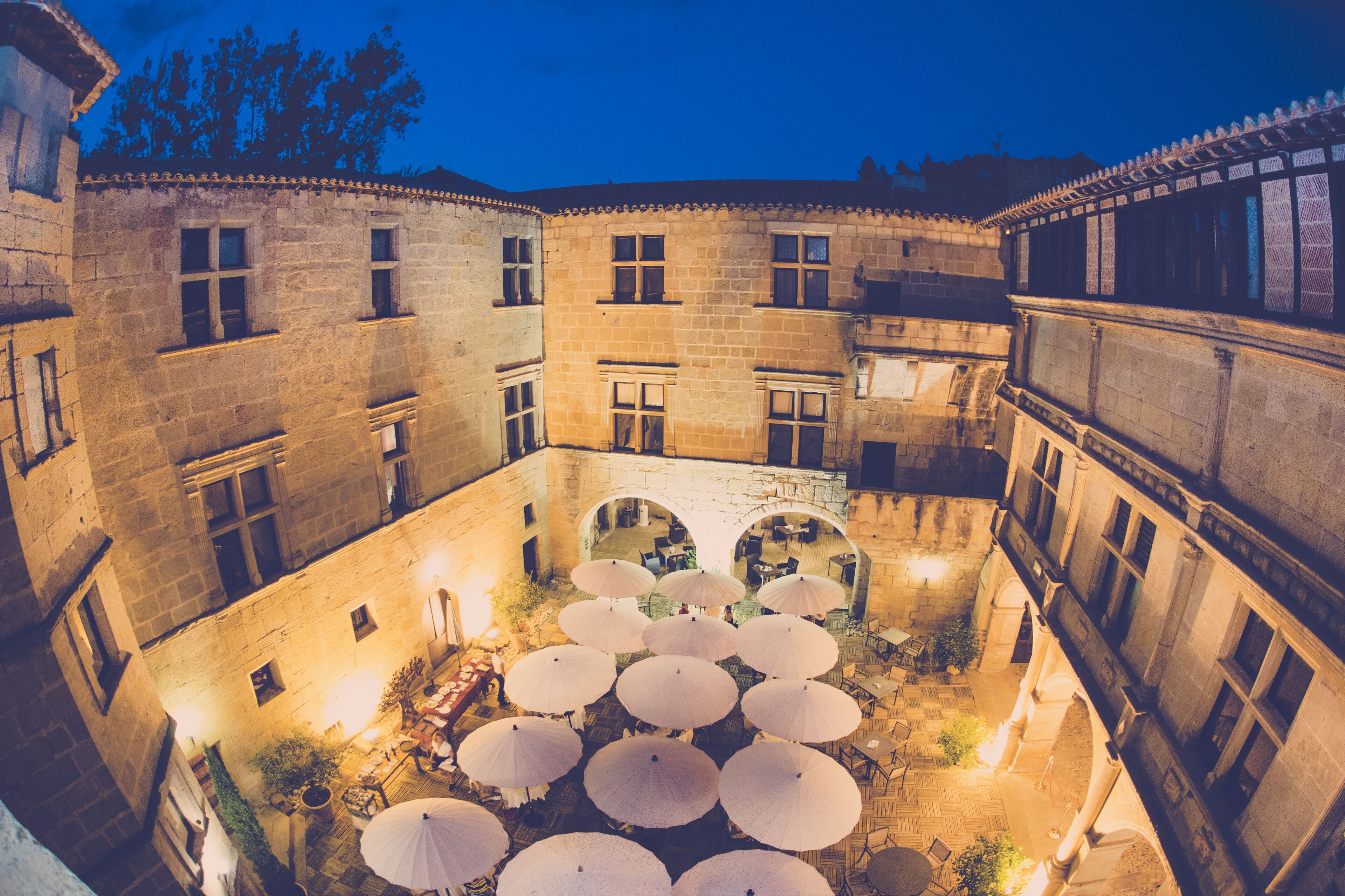 A courtyard with stone buildings, multiple umbrellas, and outdoor seating.