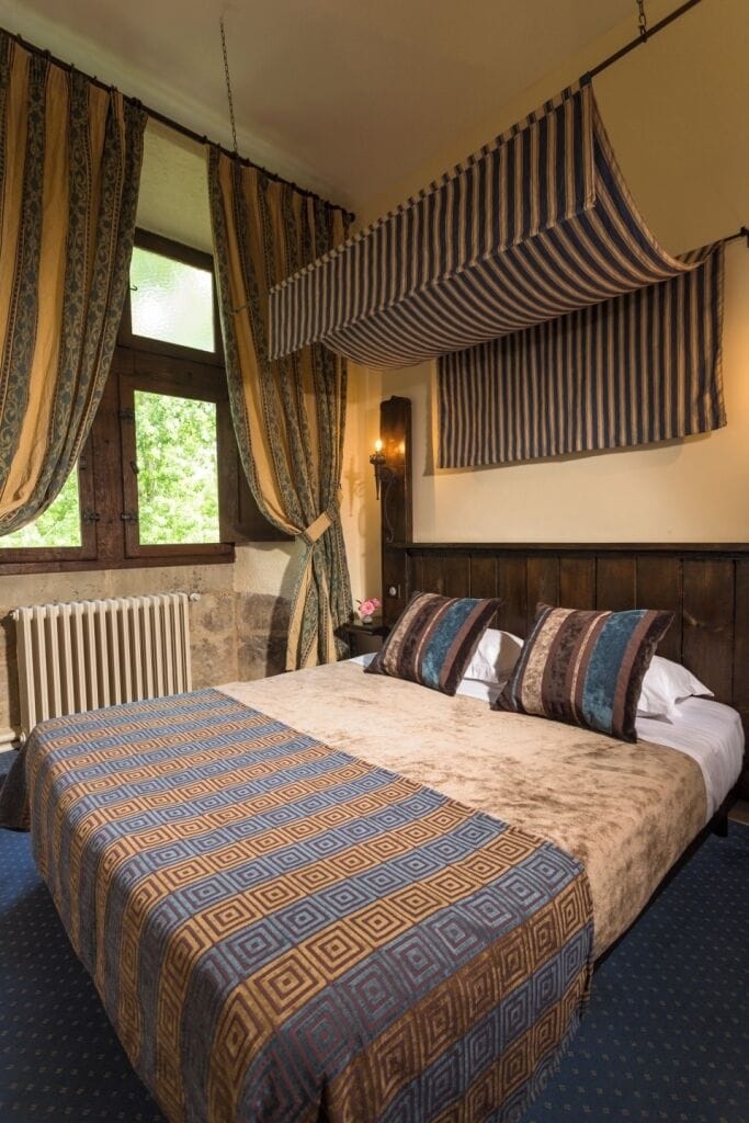 Une chambre à coucher avec un grand lit, une couvre-lit à motifs, des rideaux, un radiateur et une fenêtre.