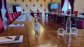 Un salón de conferencias con mesas largas, sillas rojas, una araña de cristal y una pantalla de televisión.