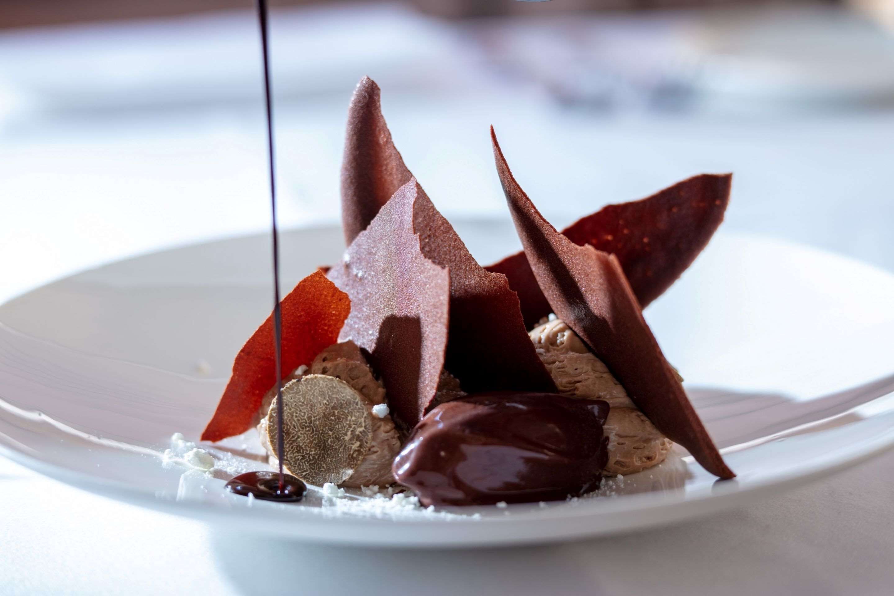 Een dessert op een wit bord met verschillende chocoladestukjes en chocoladesaus.
