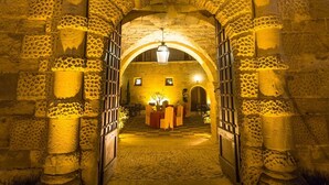 Un arco de piedra conduce a una habitación con una mesa y sillas, iluminada por una lámpara colgante.
