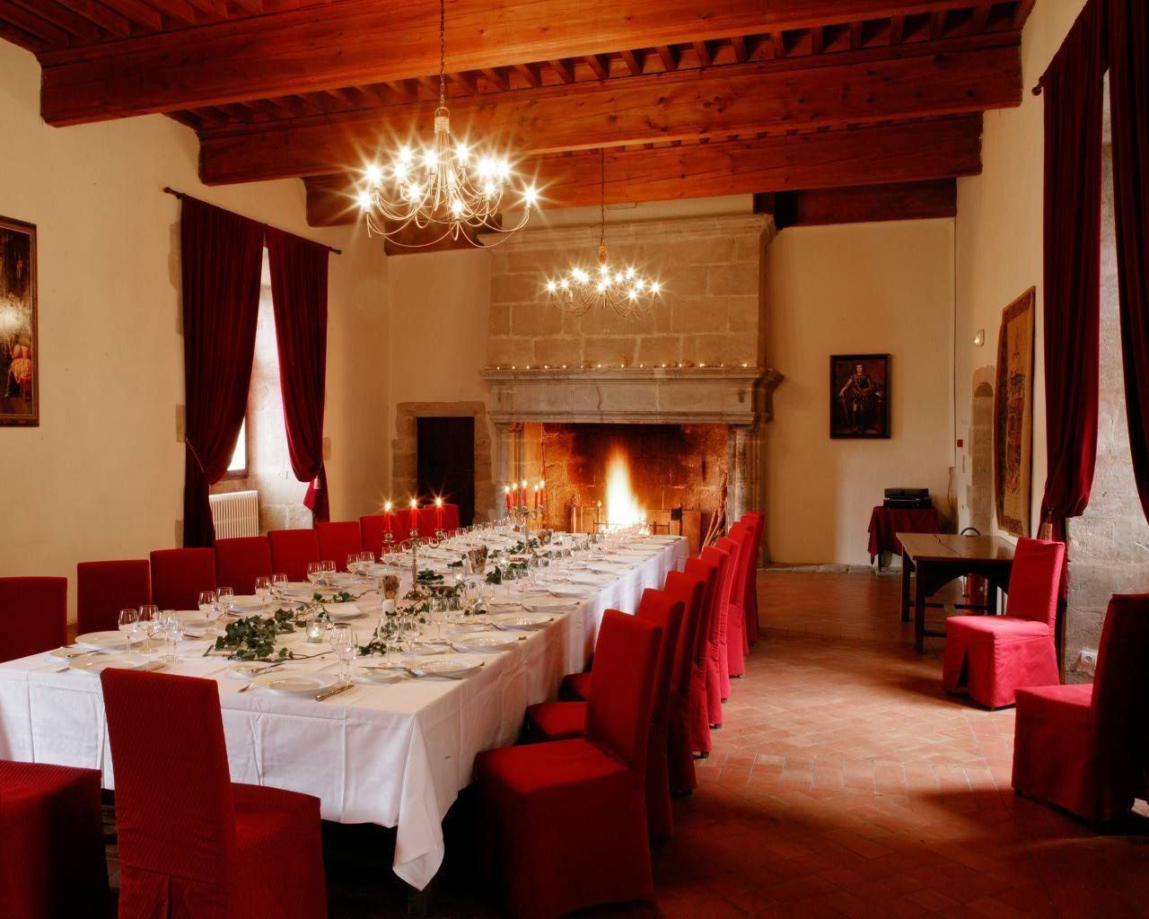 A long dining table set for a meal with red chairs, a fireplace, and a chandelier.