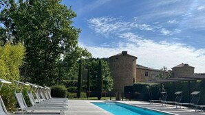 Una piscina con sillones de descanso, un edificio de piedra y cielo despejado.