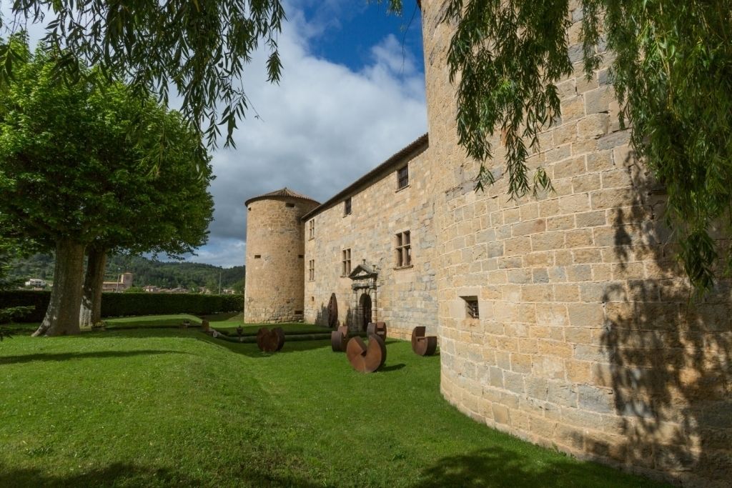 A historic stone building with a round tower, surrounded by well-maintained grass and trees.