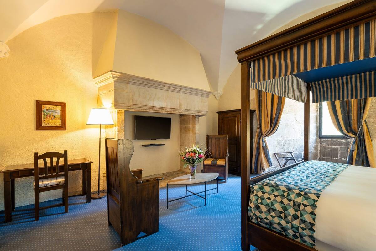 A hotel room with a bed, a desk, a chair, a TV, and a fireplace.