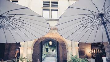 Une entrée en arc surmontée de parasols, des marches en pierre et une vue sur l’intérieur d’un bâtiment.