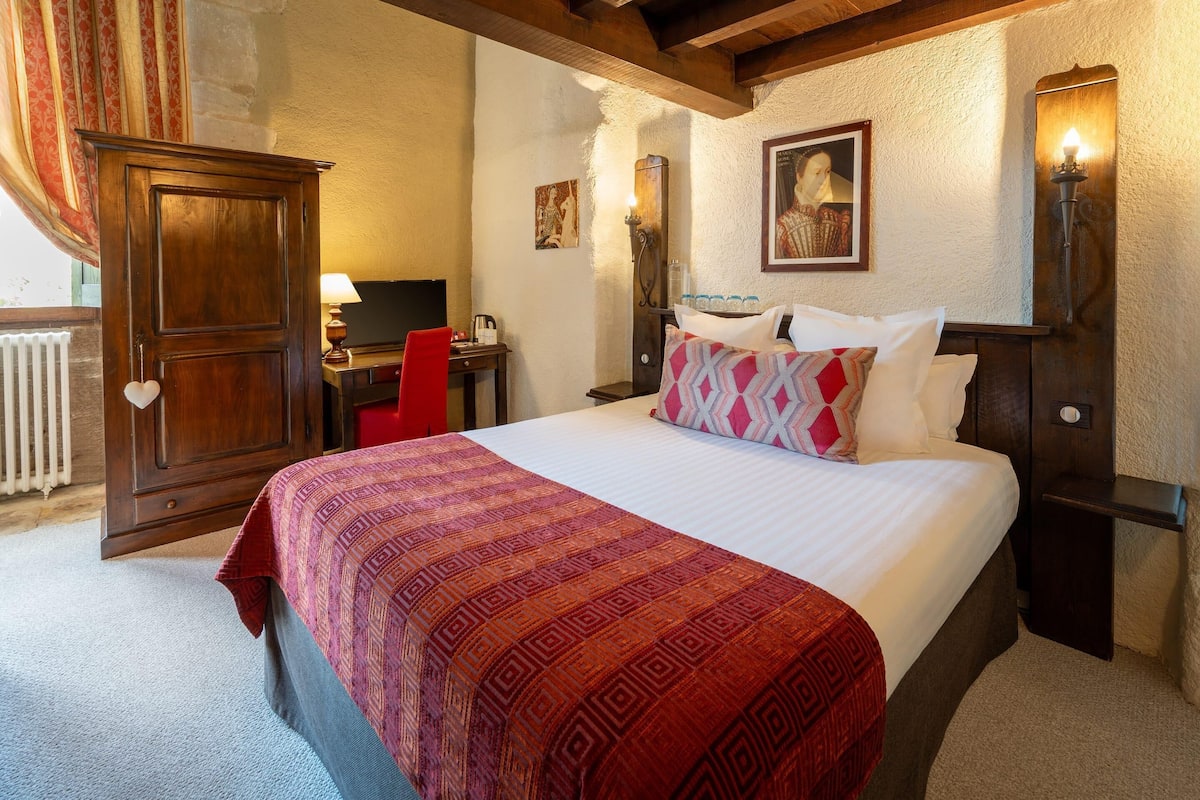 A bedroom with a large bed, a wooden wardrobe, a desk with a chair, and a radiator.
