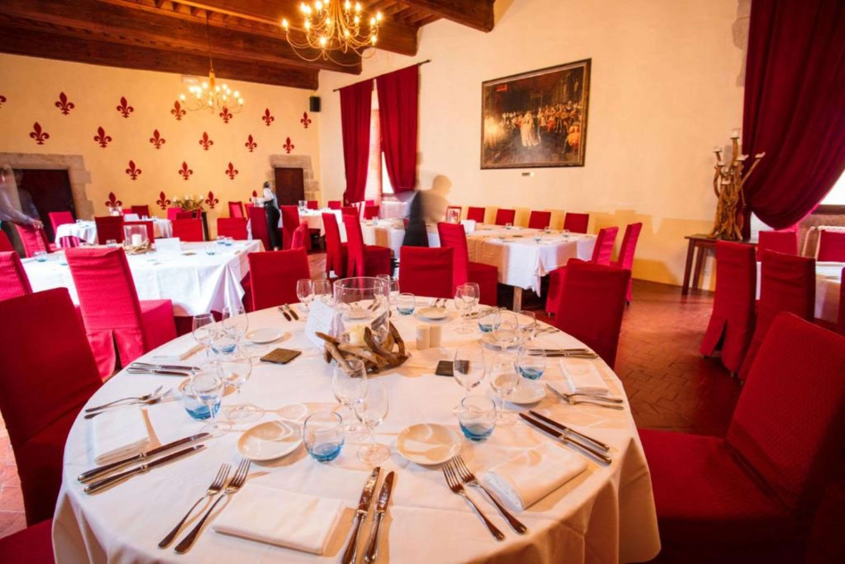 Un restaurante con mesas redondas dispuestas para comer, sillas rojas y una lámpara de araña.