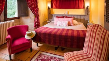 Um quarto aconchegante com uma cama, uma poltrona vermelha, uma cadeira listrada e um chapéu decorativo na poltrona.