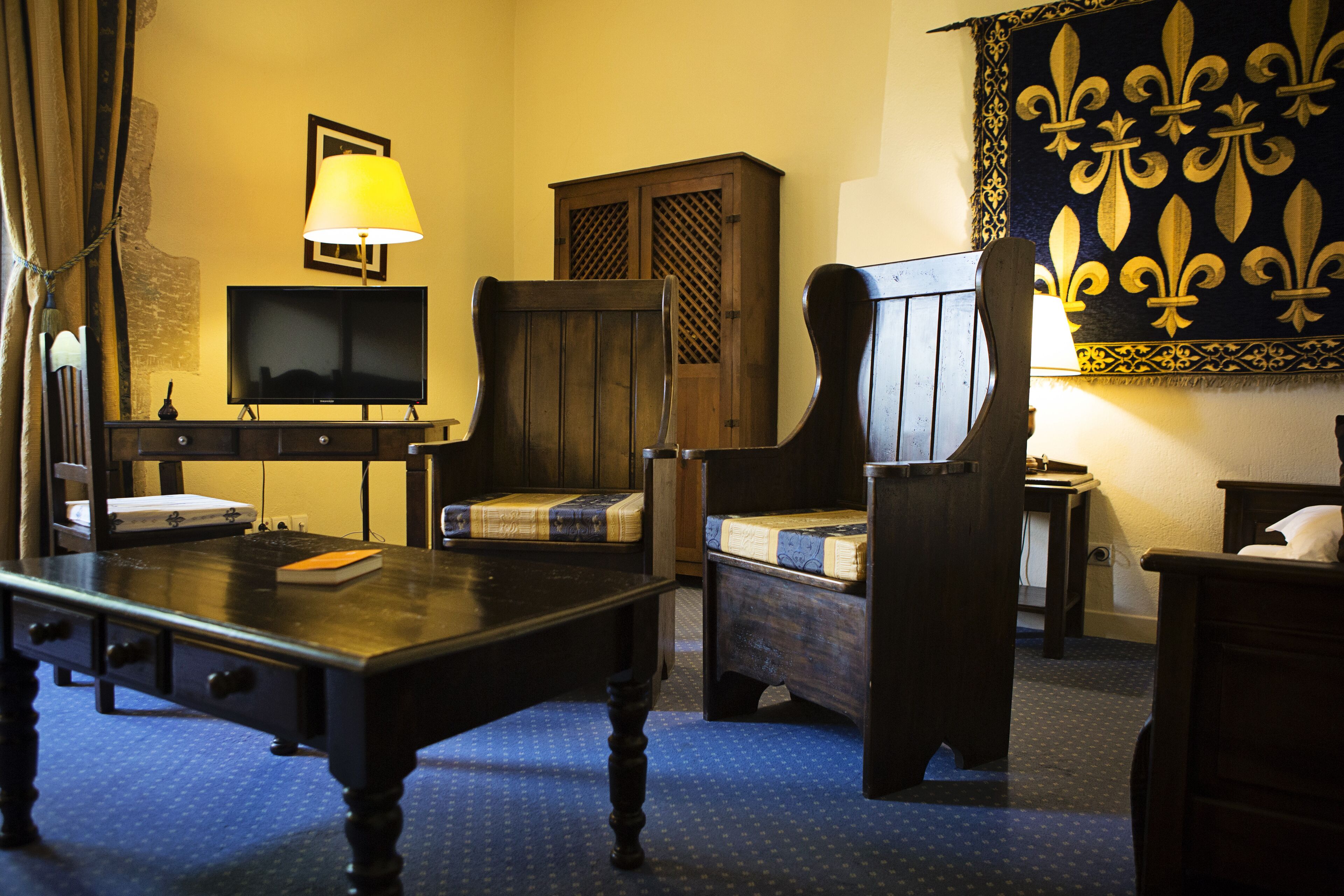Habitación de hotel con un escritorio de madera, televisión, silla, cama y un tapiz decorativo.