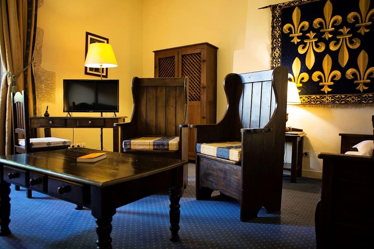 A room with a wooden desk, a television, a chair, a cabinet, and a patterned wall hanging.