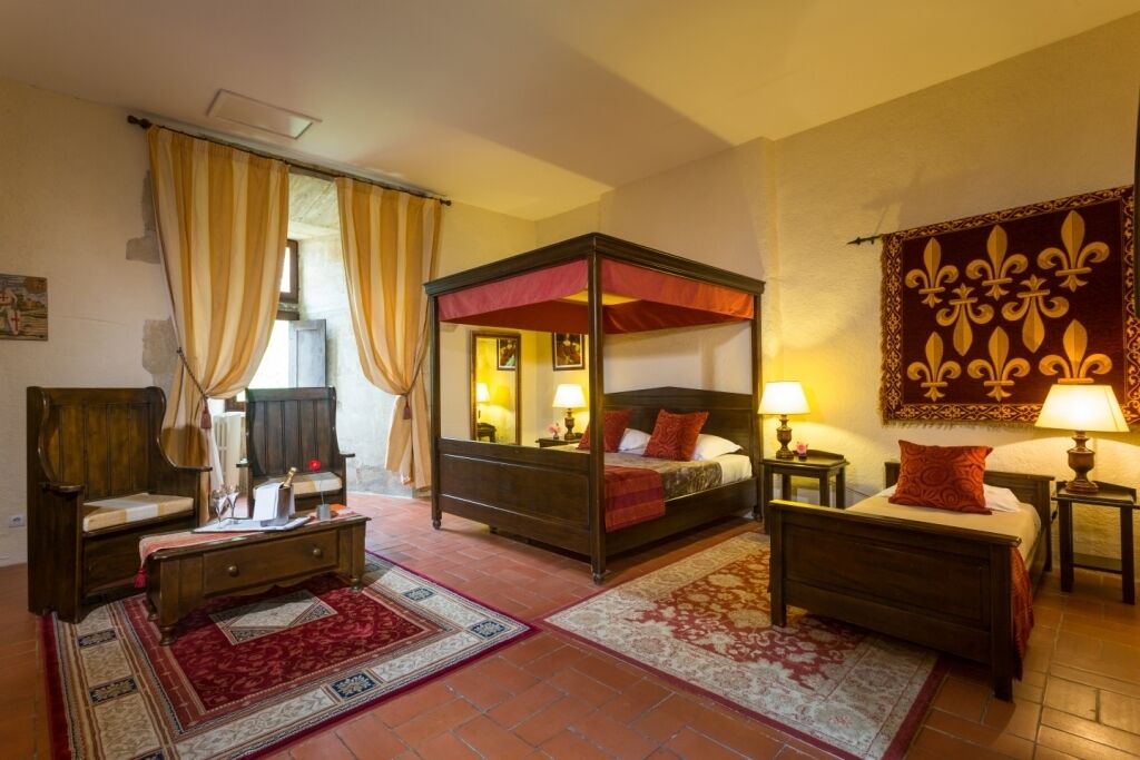 A four-poster bed with a canopy, a wooden nightstand, a bedside table, and a red and white patterned rug.