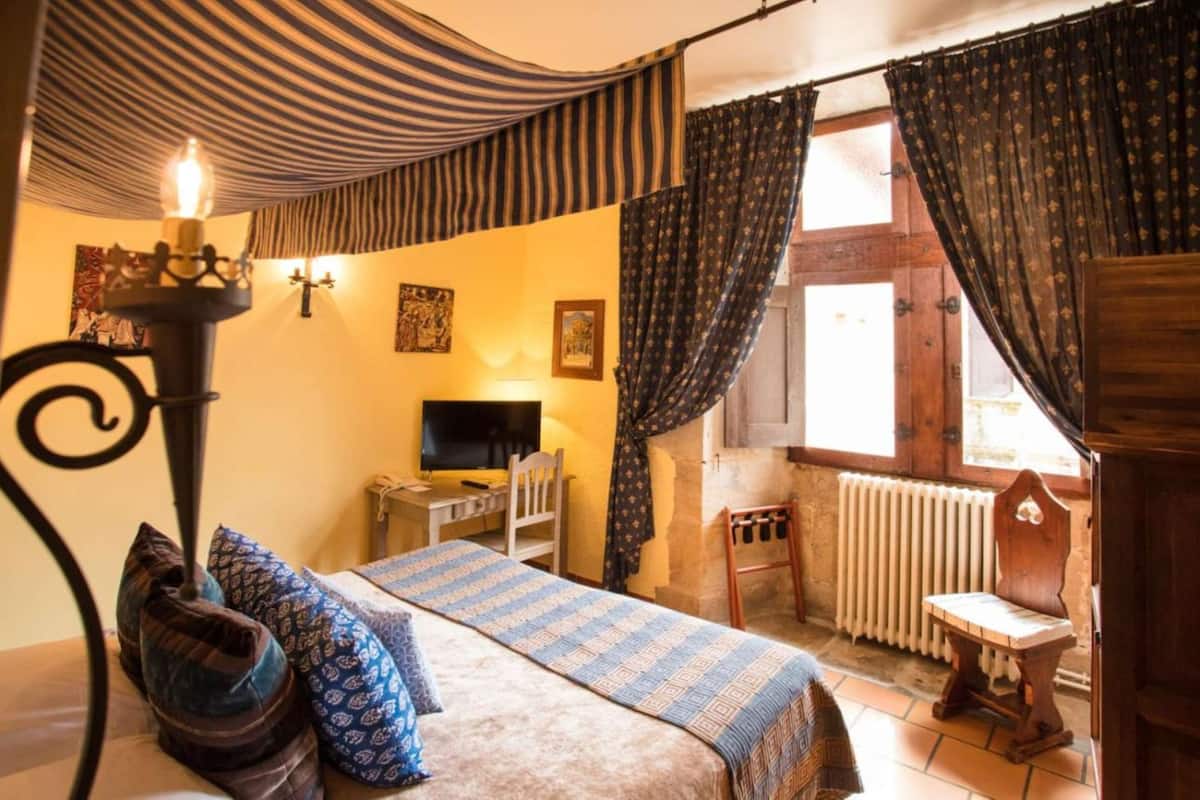 A cozy room with a bed, a desk, a chair, a radiator, and a window with curtains.