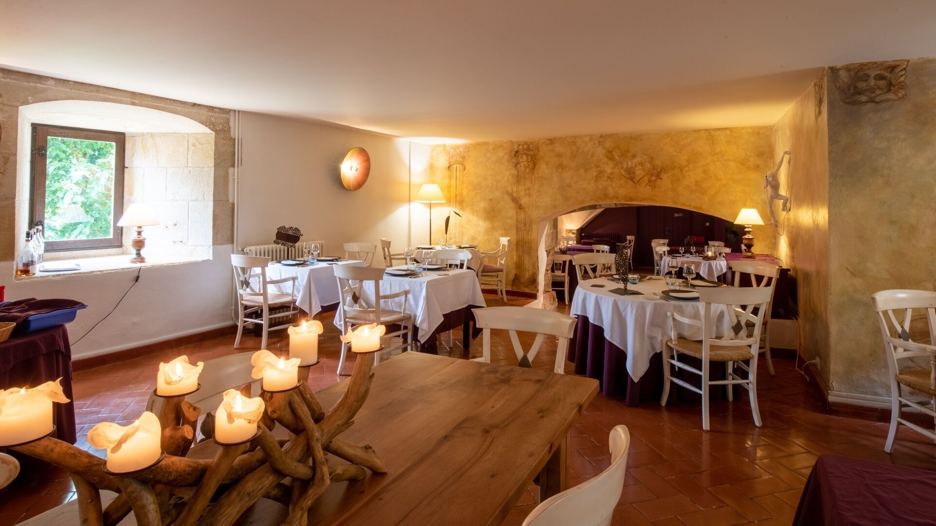 A dining area with multiple tables set for guests, a fireplace, and candles providing ambient lighting.