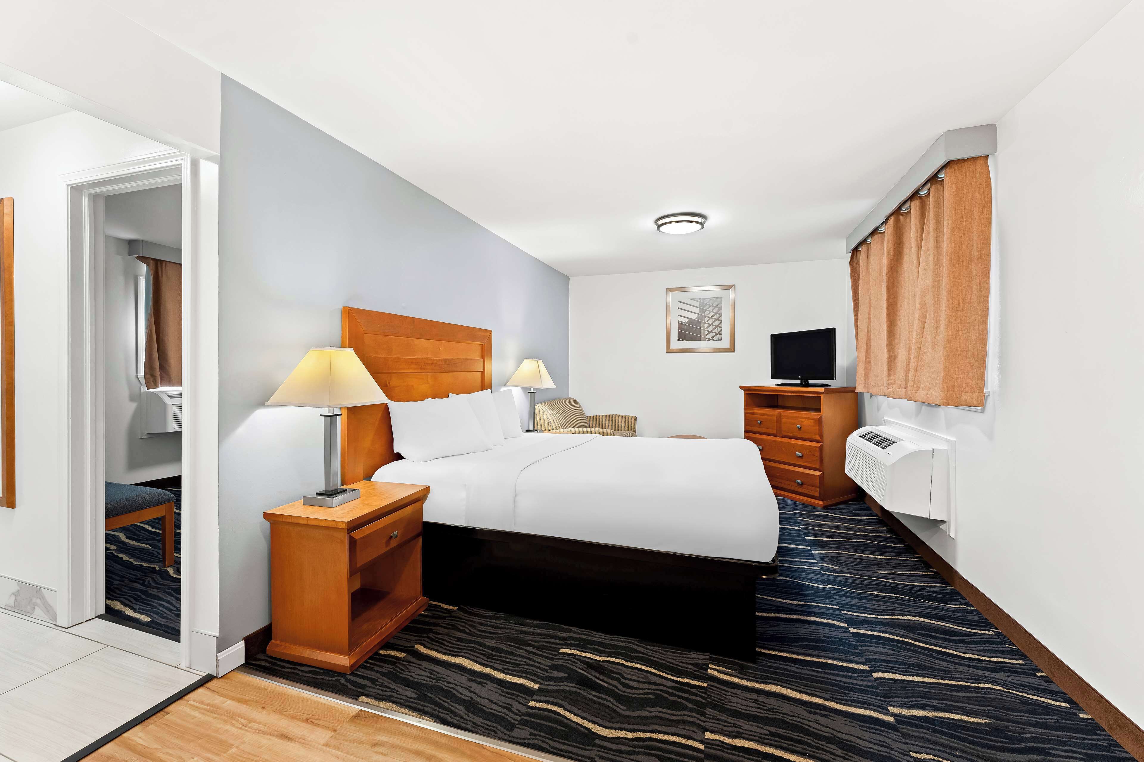Habitación de hotel con cama, mesitas de noche, lámpara, televisor y equipo de aire acondicionado.