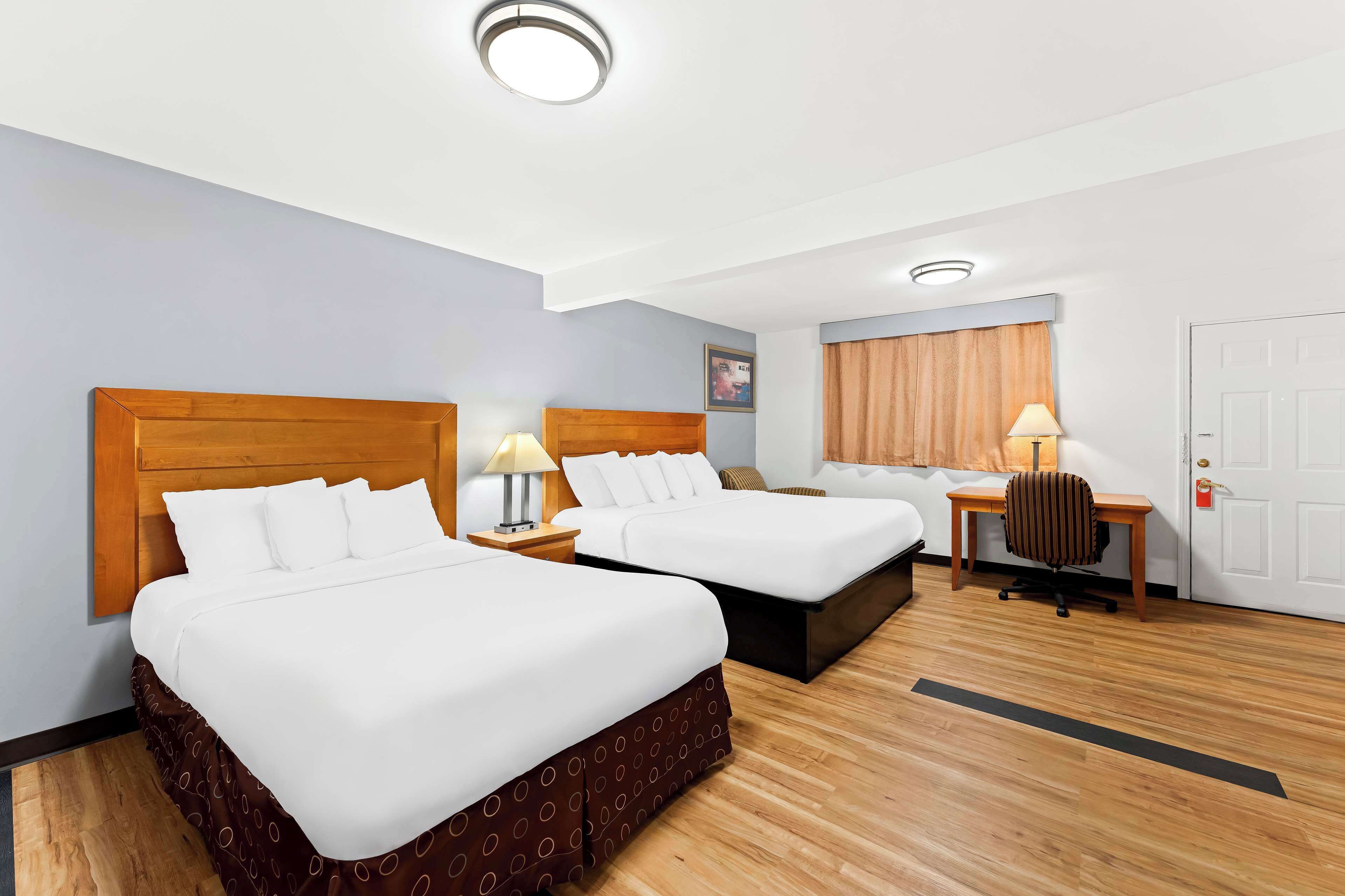 A hotel room with two beds, a desk, a chair, and a door.
