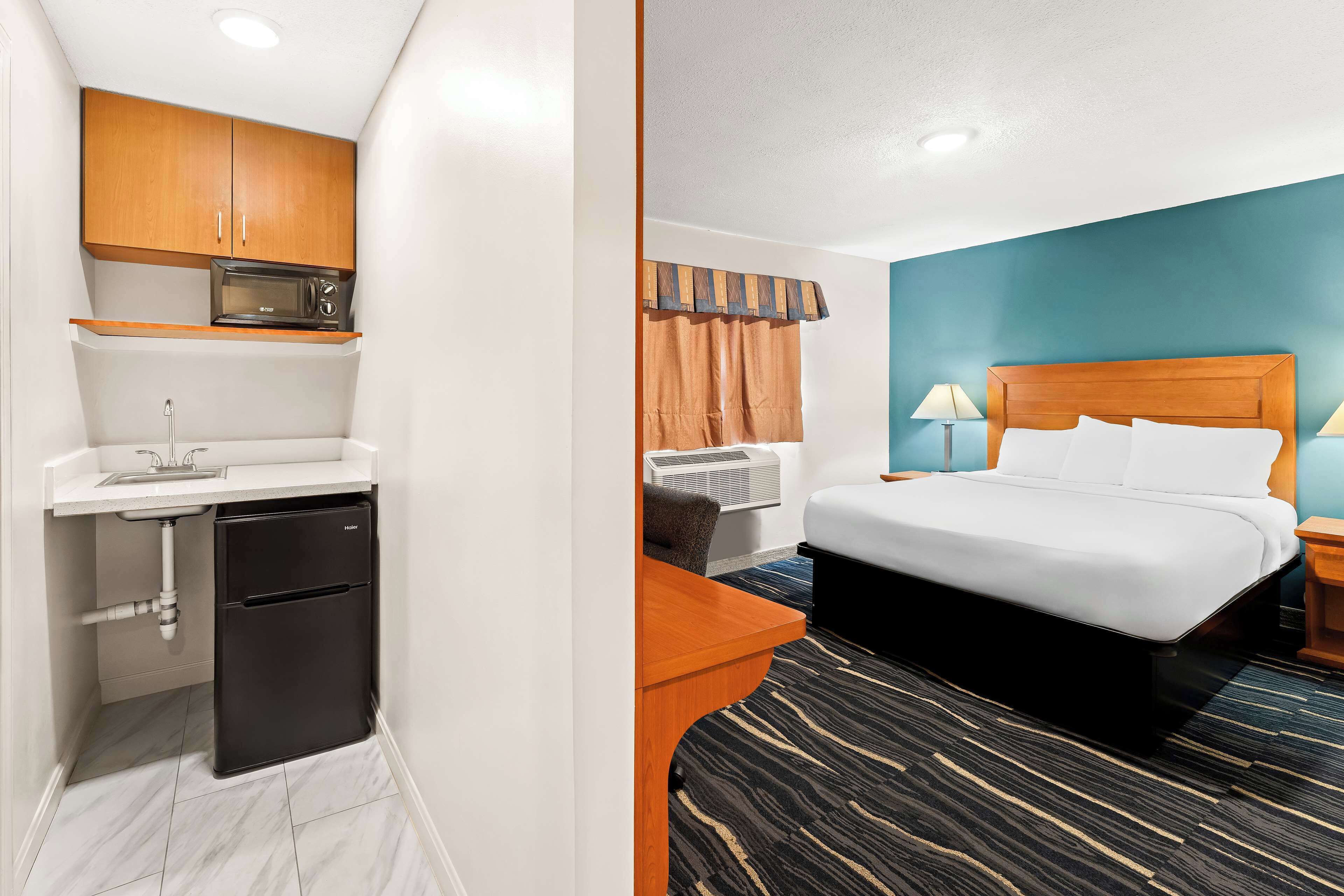 A compact room with a kitchenette, a bed, and a window with curtains.