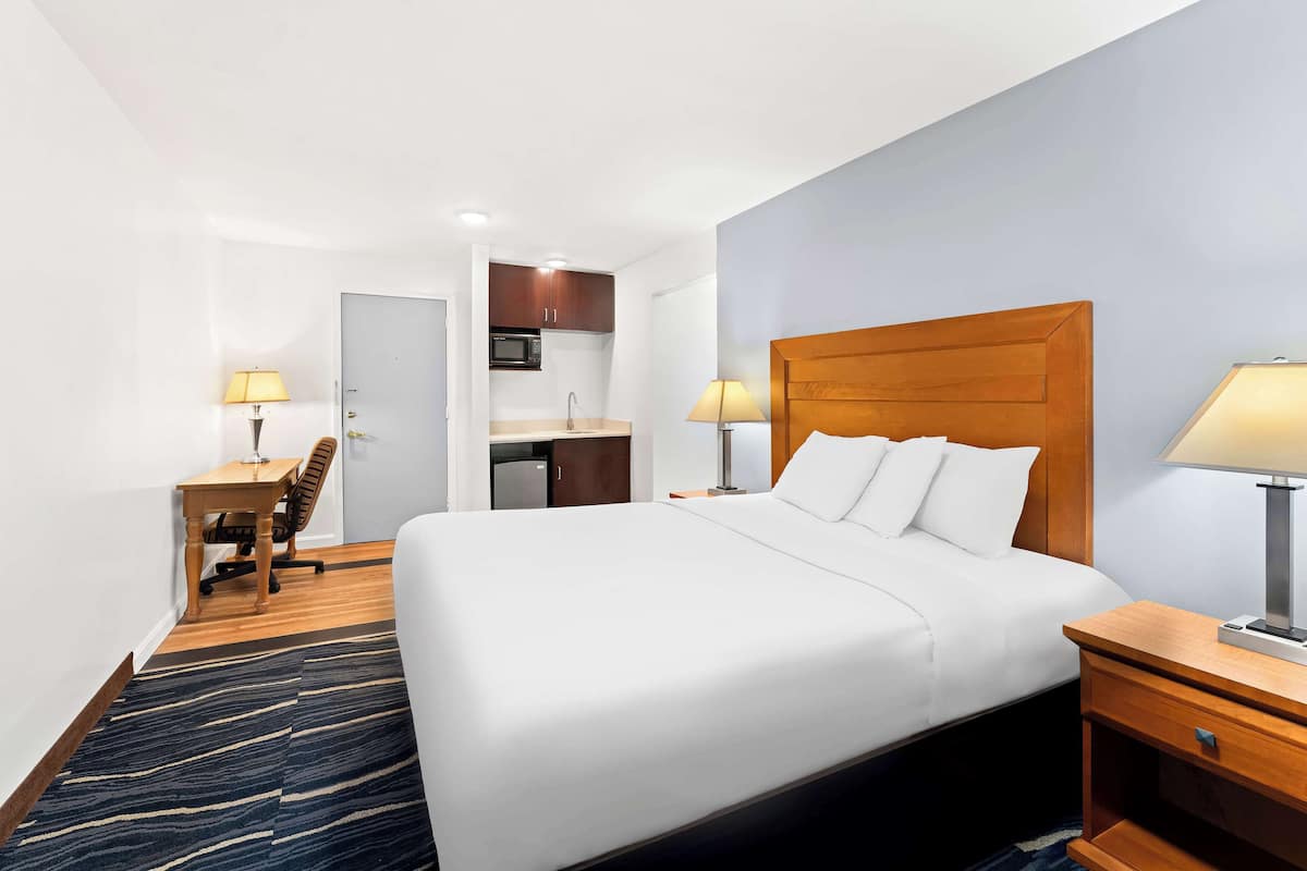 A hotel room with a large bed, a desk with a chair, a kitchenette, and a bathroom.