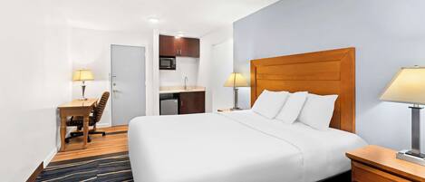 Una habitación de hotel con una cama grande, un escritorio con silla, una kitchenette y un baño.