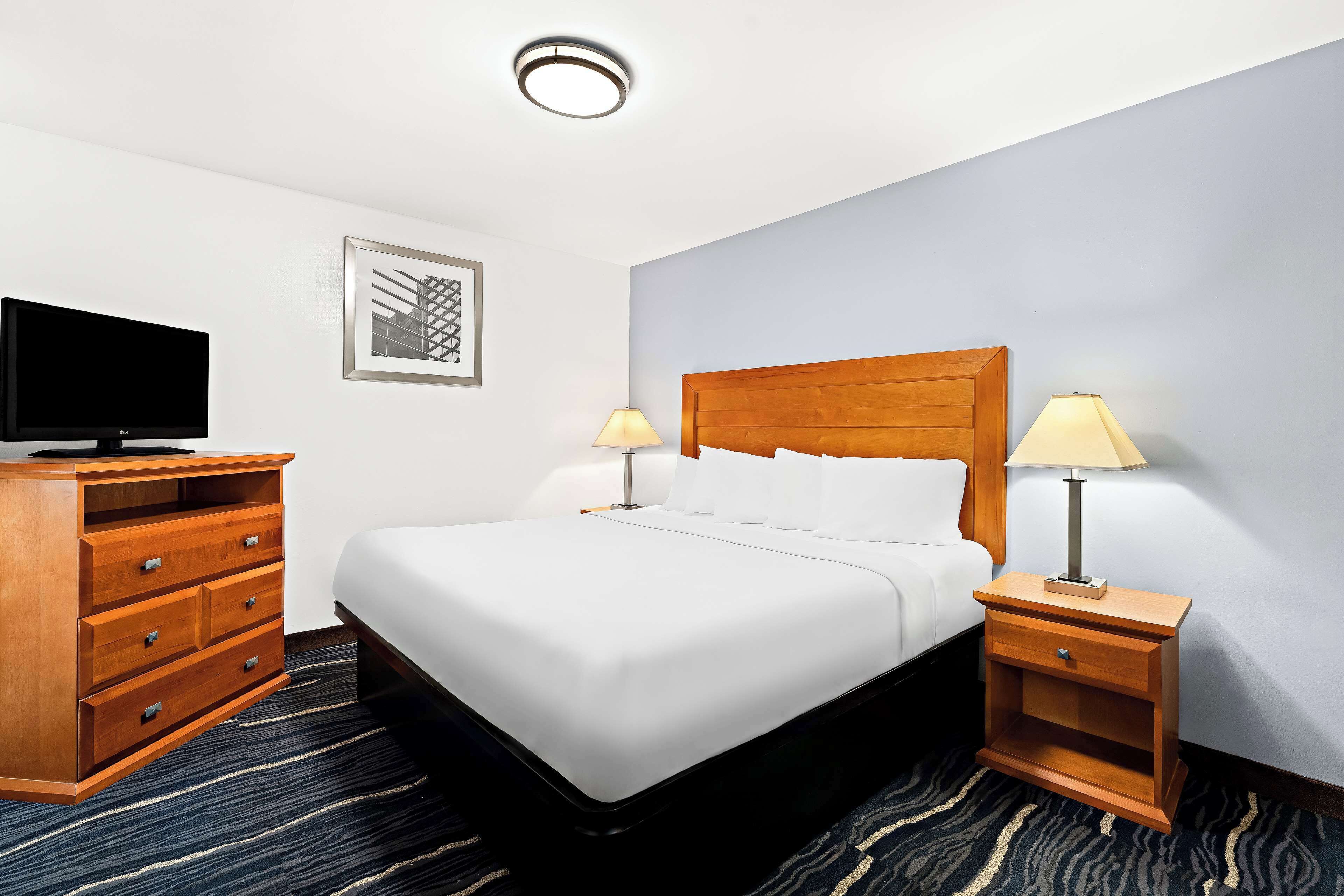 A hotel room with a bed, a TV, a wooden dresser, and two bedside lamps.