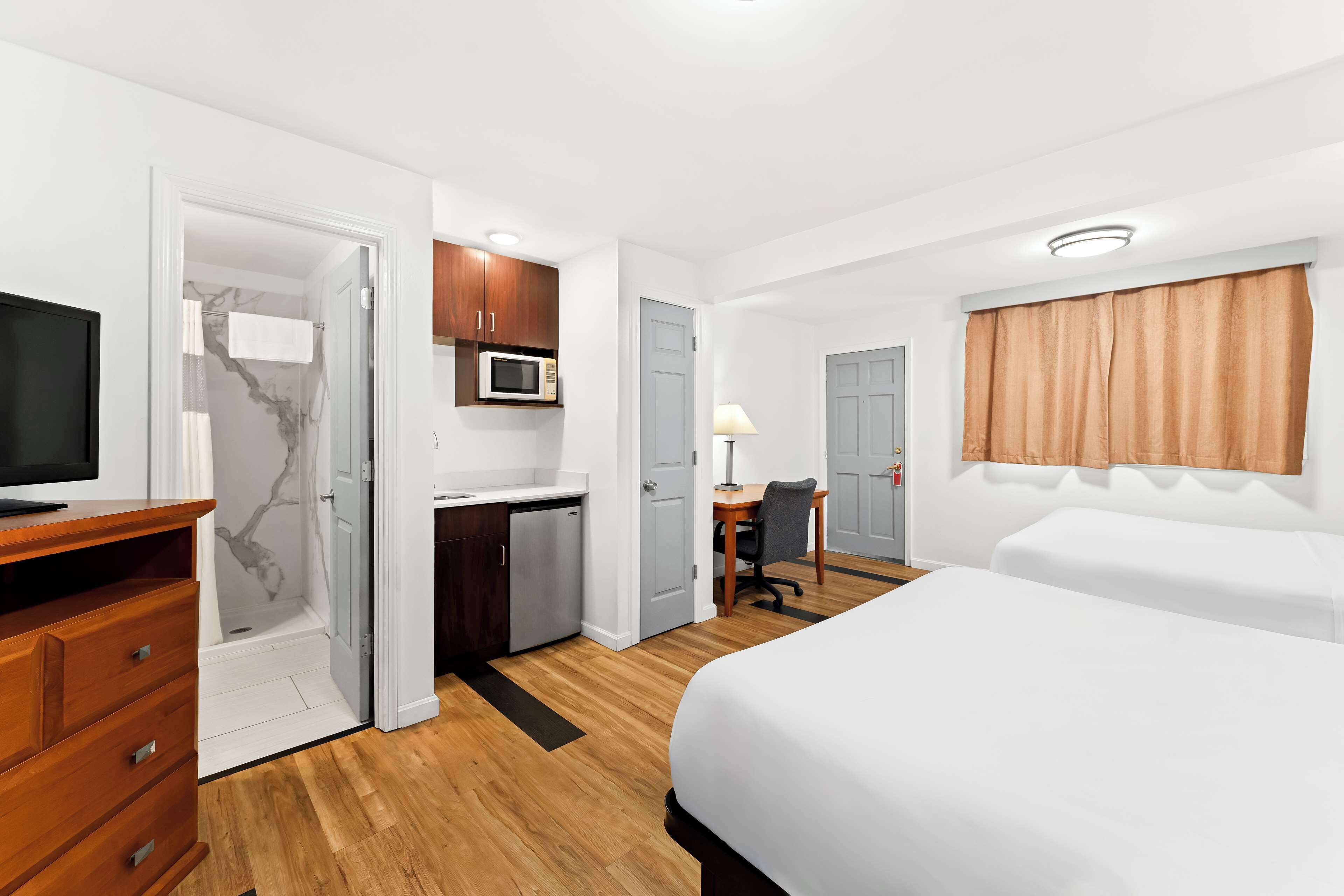 A hotel room with a bed, a desk, a microwave, a TV, and a shower.
