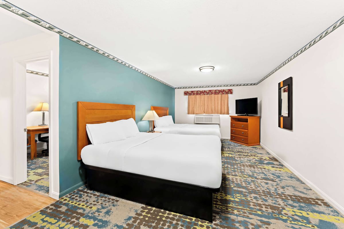 A hotel room with a large bed, a desk, a television, and a patterned carpet.