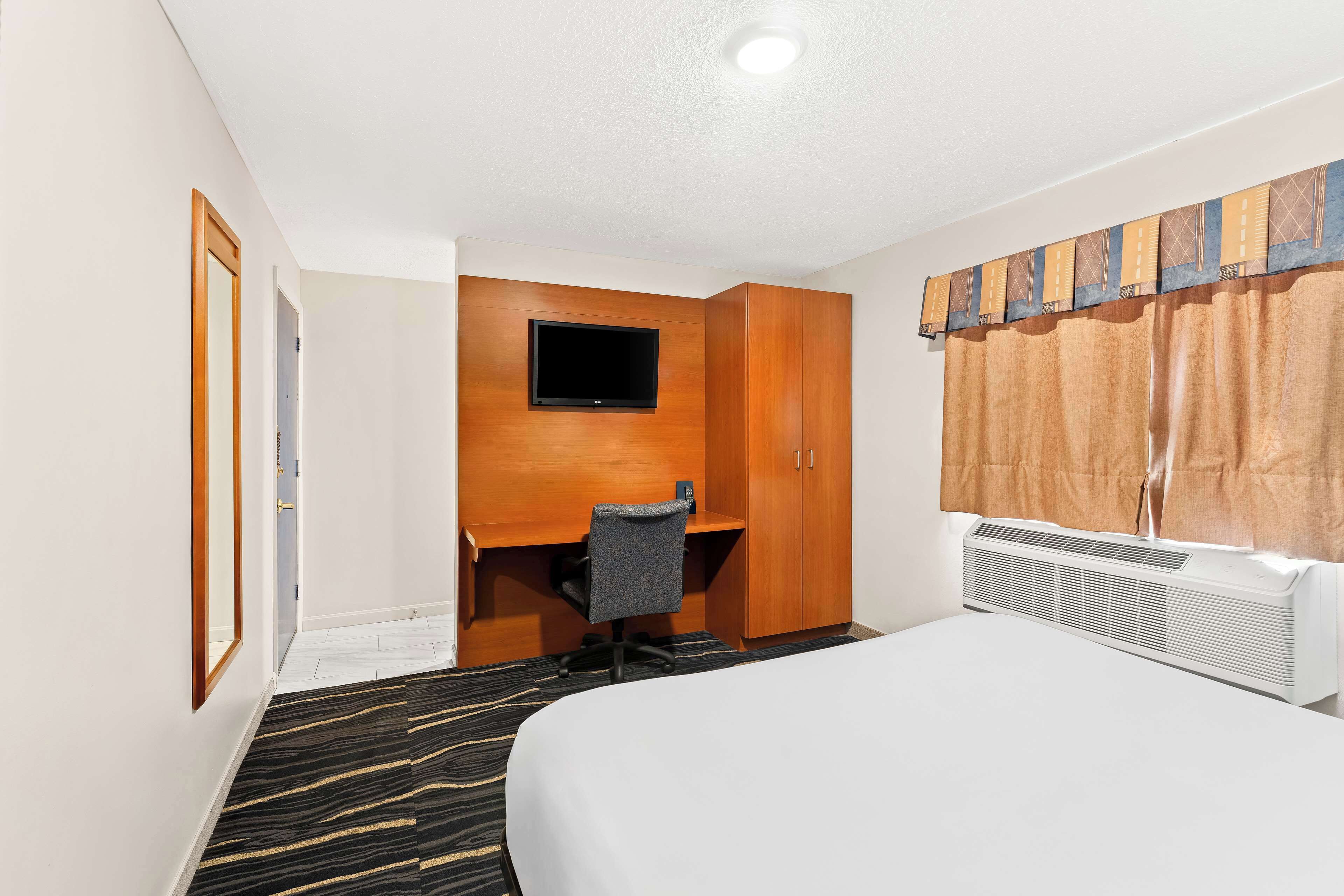 Ein Hotelzimmer mit Bett, Schreibtisch mit Stuhl, Fernseher und einem Fenster mit Vorhängen.