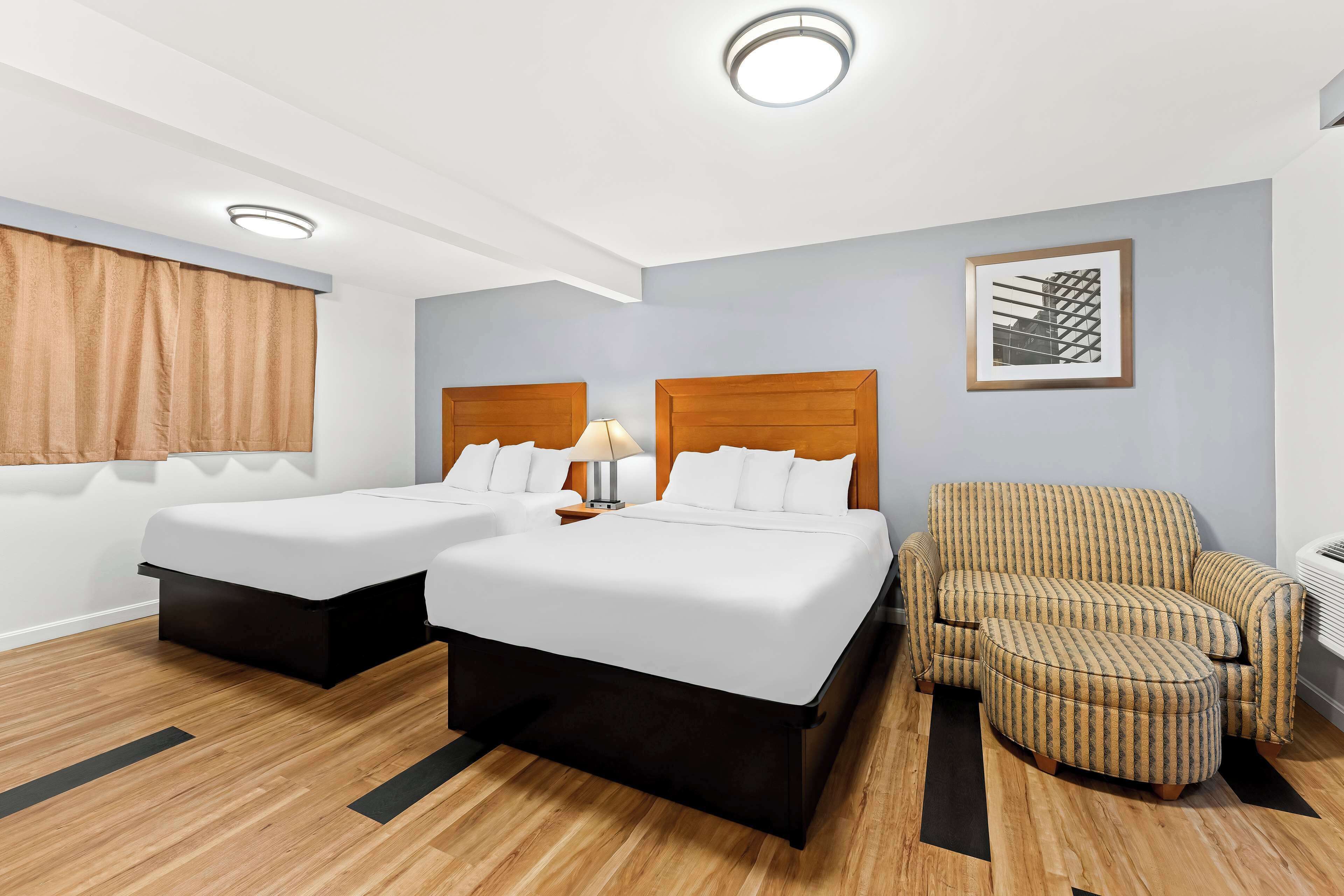 A hotel room with two beds, a chair, and a lamp.