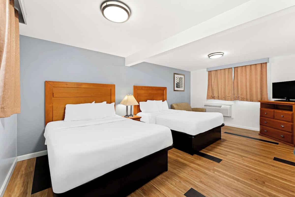 A hotel room with two beds, a desk, a TV, and a bathroom.