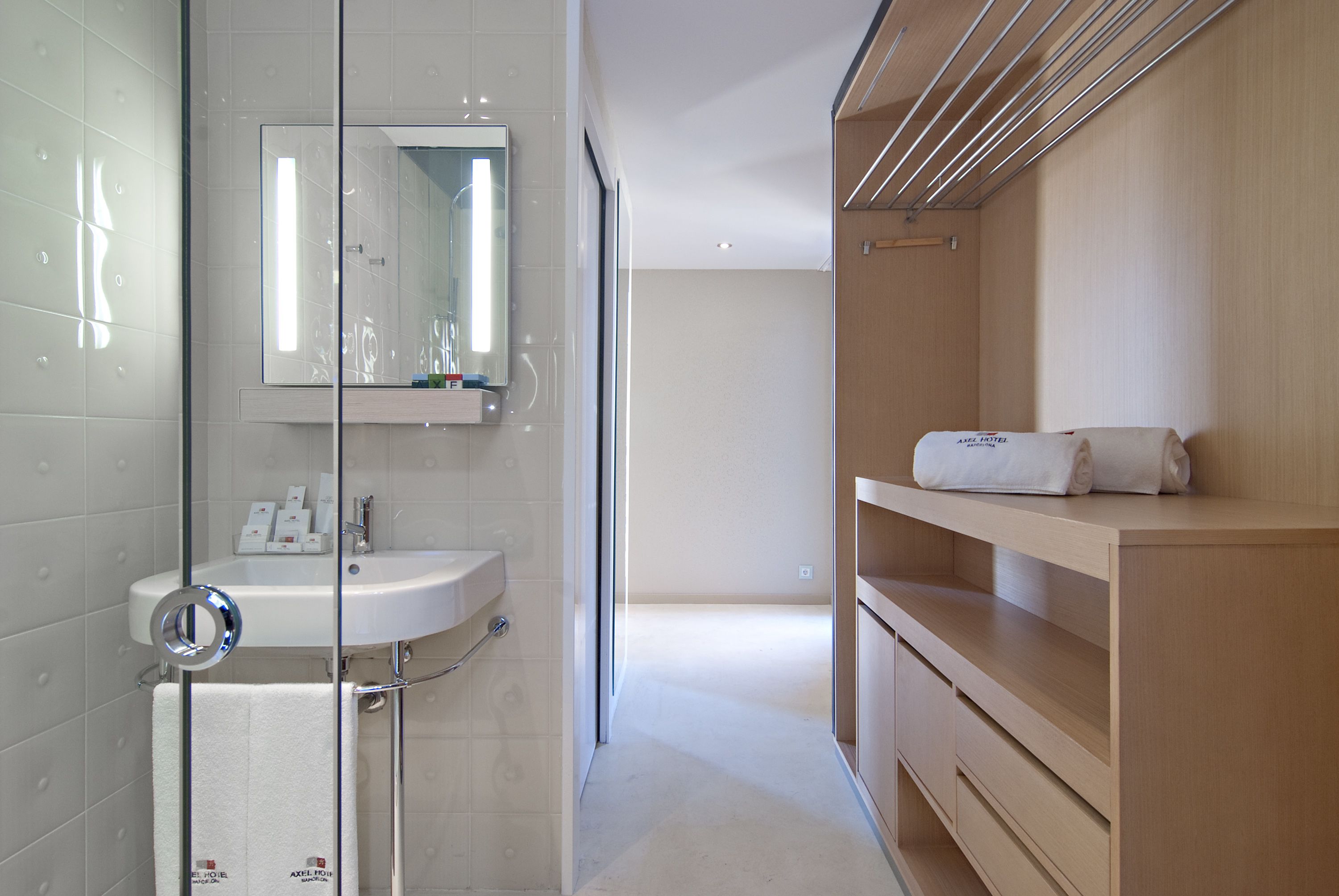 Un baño moderno con cabina de ducha de vidrio, un lavabo blanco y un mueble de tocador de madera con una toalla.