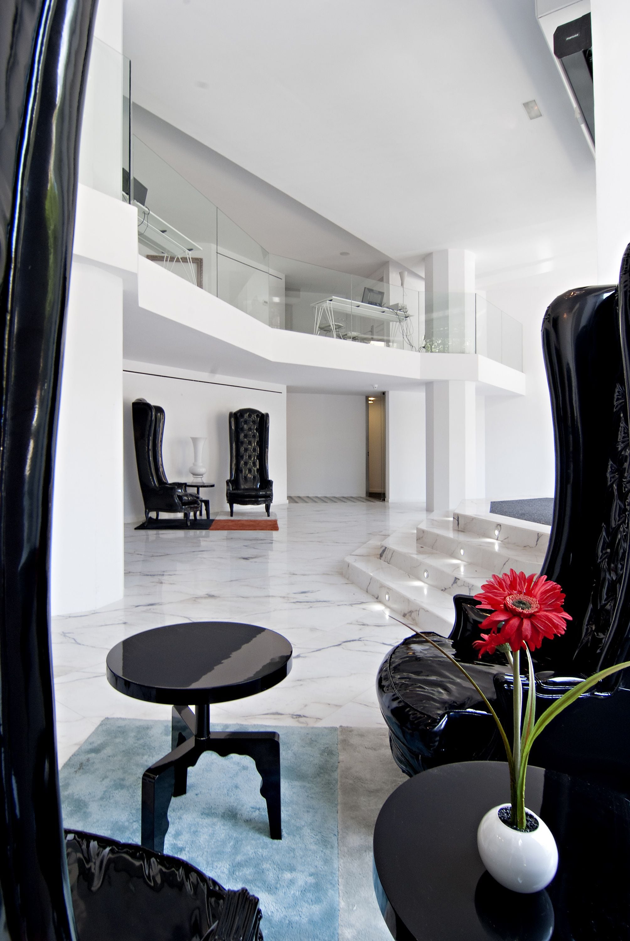 Un vestíbulo amplio con piso de mármol, muebles negros y un jarrón con una flor roja.