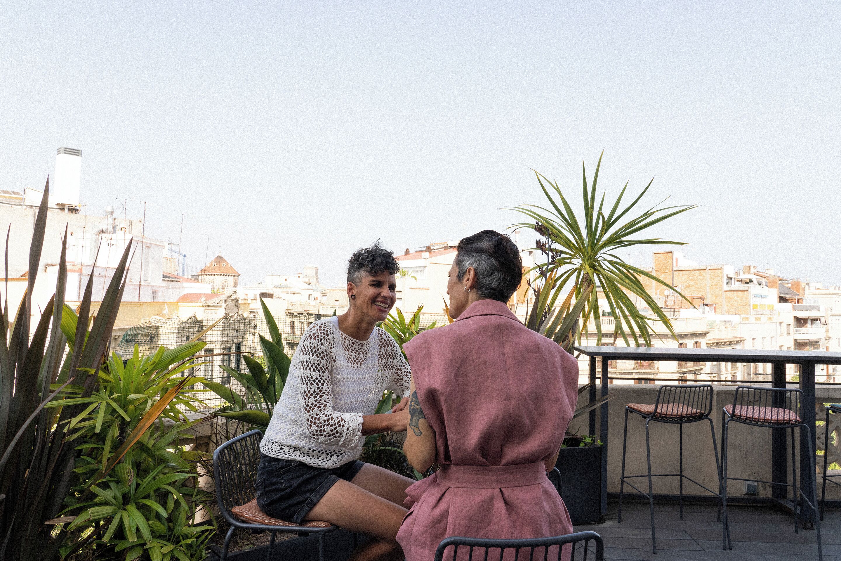Two people seated on a balcony with a cityscape view.