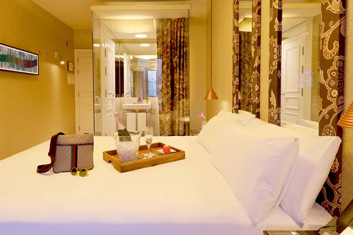 A hotel room with a bed, a tray with a bottle and glasses, and a suitcase.